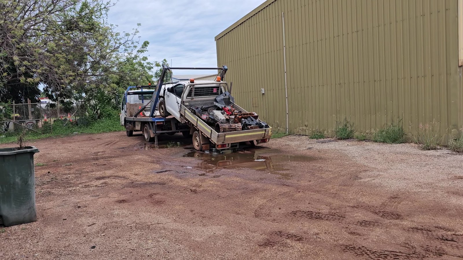 A tow truck with a ute on its tray beside the olive-green TJ Auto Tech shed