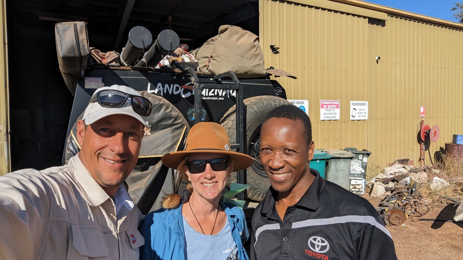 Three smiling people in the TJ Auto Tech yard with a loaded vehicle behind them