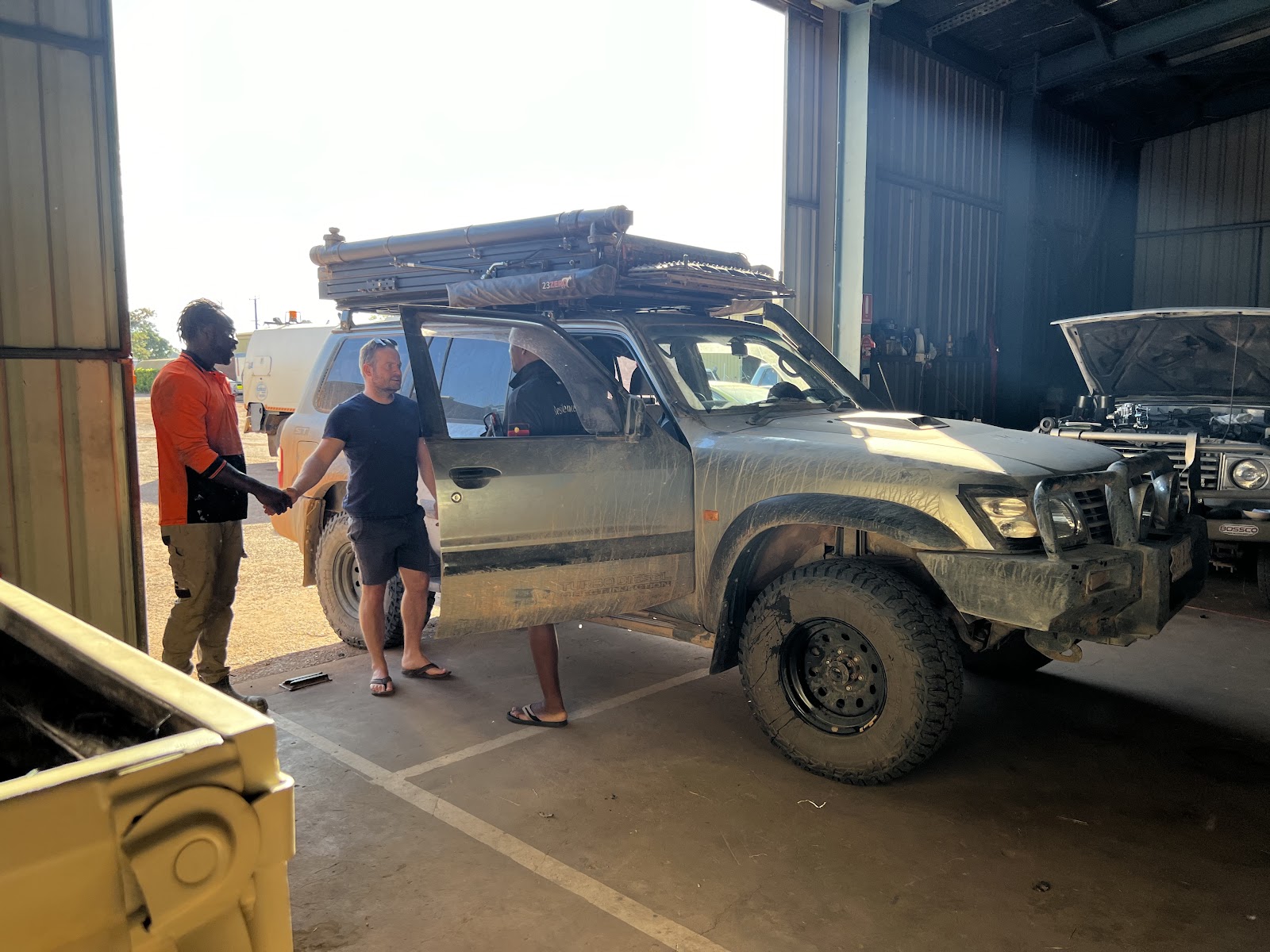 A traveller shaking hands in the TJ Auto Tech workshop beside a Nissan Patrol with a rooftop tent